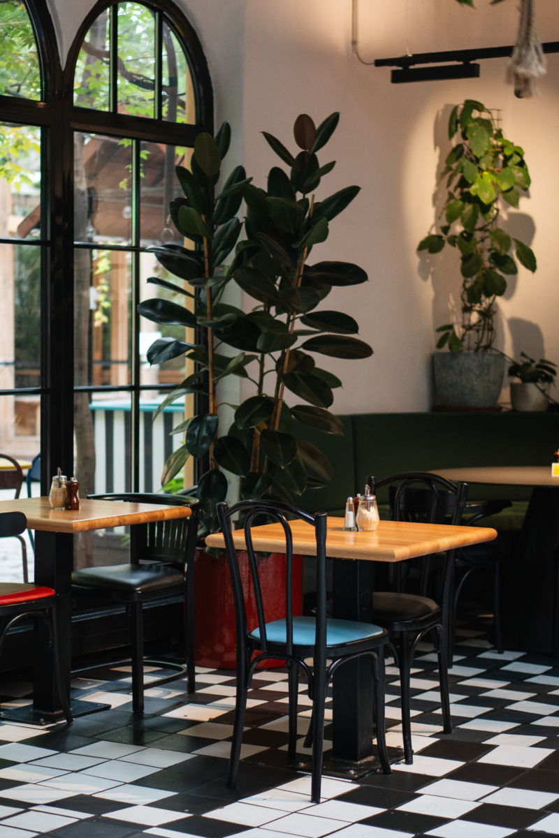 Inenraum eines Cafes, schwarz-weiße Bodenfliesen, Cafehaustische mit Holztischplatte und schwarzen Stühlen, große bodenlange Fenster