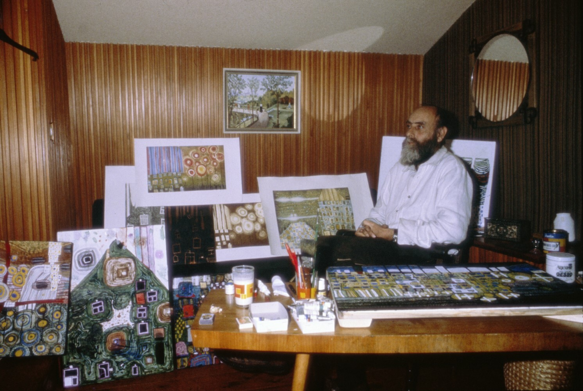 Hundertwasser in einem Raum sitzend umgeben von seinen eigenen Bildern
