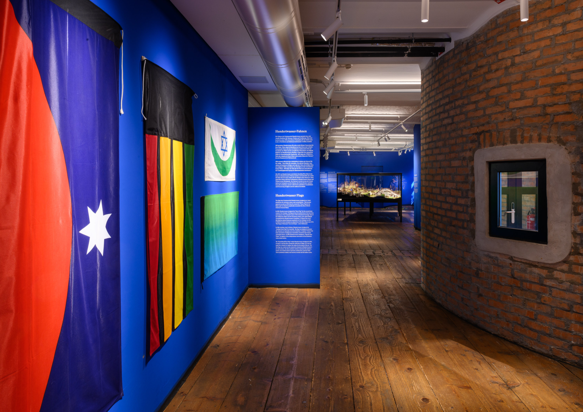 Einblick in den Ausstellungsraum, Holzboden und blaue Wände mit Fahnen