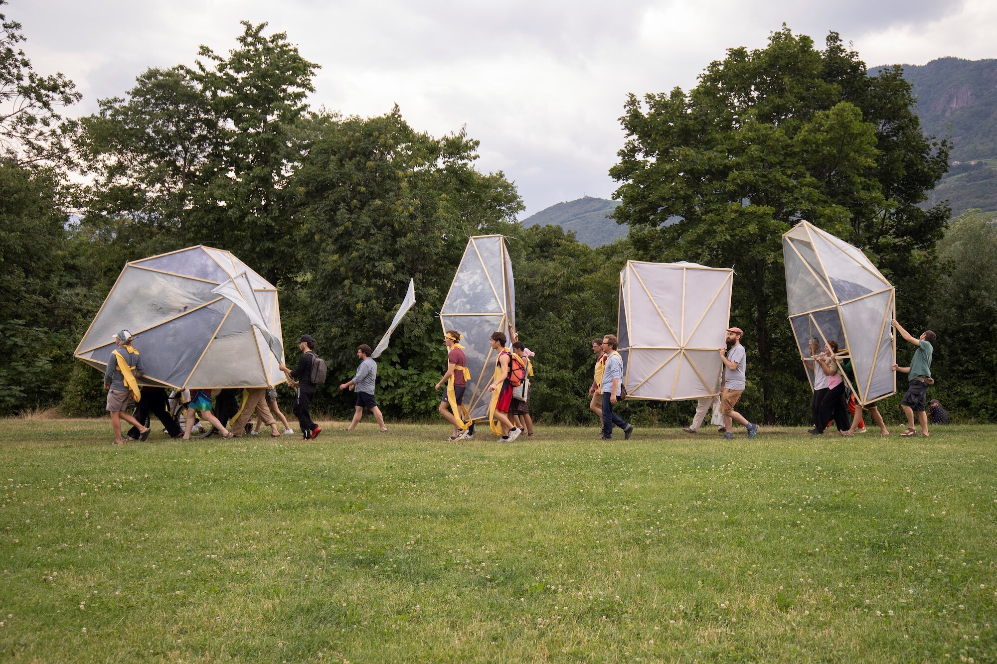 Eine Gruppe von Menschen tragen mehrere überdimensionale Schirme über eine Wiese